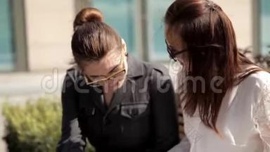 两个年轻的商业女孩在商业中心附近的公园进行商业谈判，分享商业想法